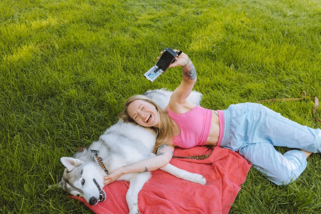 Woman With Dog Lying On Grass and Taking a Selfie